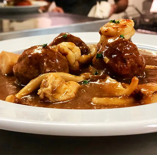 A white plate of meatballs in a brown sauce with cuttlefish and grilled shrimp, Ca l'Estevet