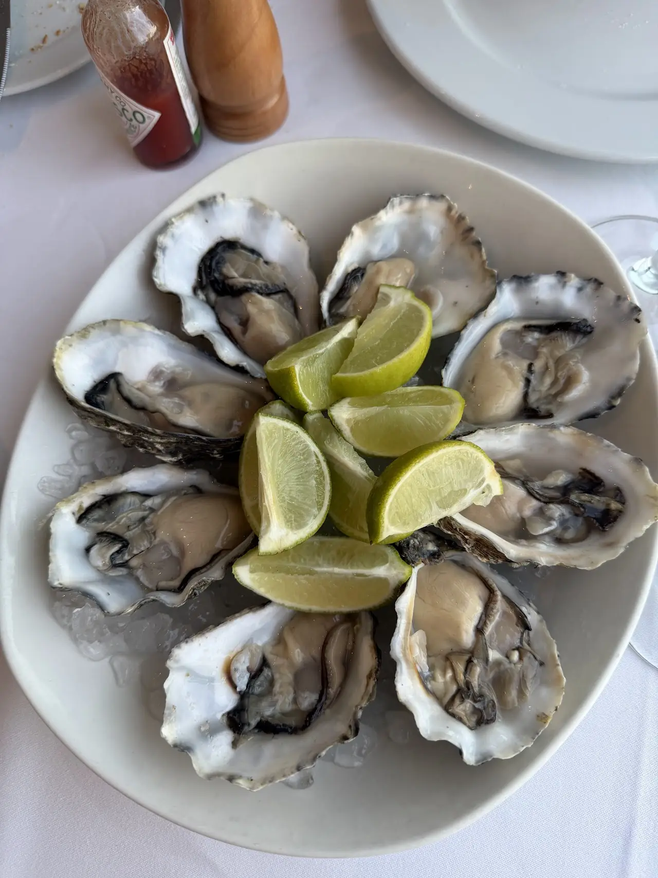 A plate of half-shell oysters served with lime wedges.
