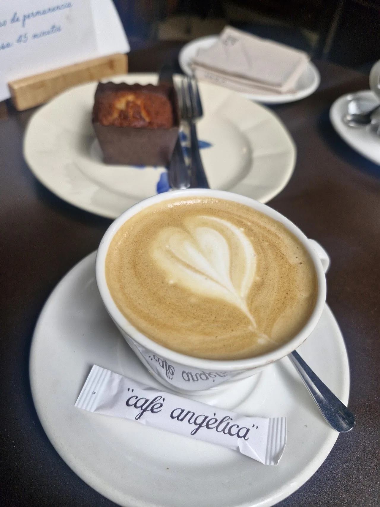 A latte with a heart pattern beside a slice of chocolate loaf cake