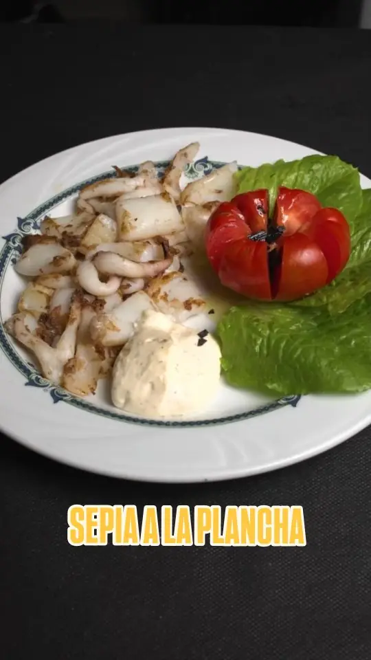 Grilled cuttlefish strips on a plate with alioli and a halved grilled tomato on lettuce