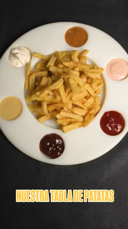 Basket of french fries on a white plate surrounded by six different dipping sauces