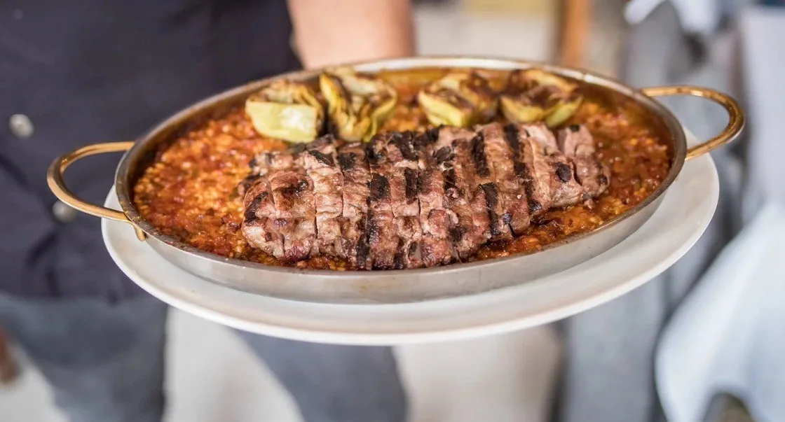 A paella-style pan of rice topped with sliced grilled steak