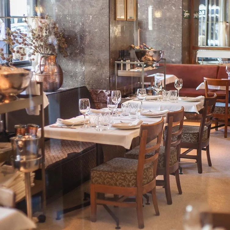 A dining room with tables set with white tablecloths and wooden chairs