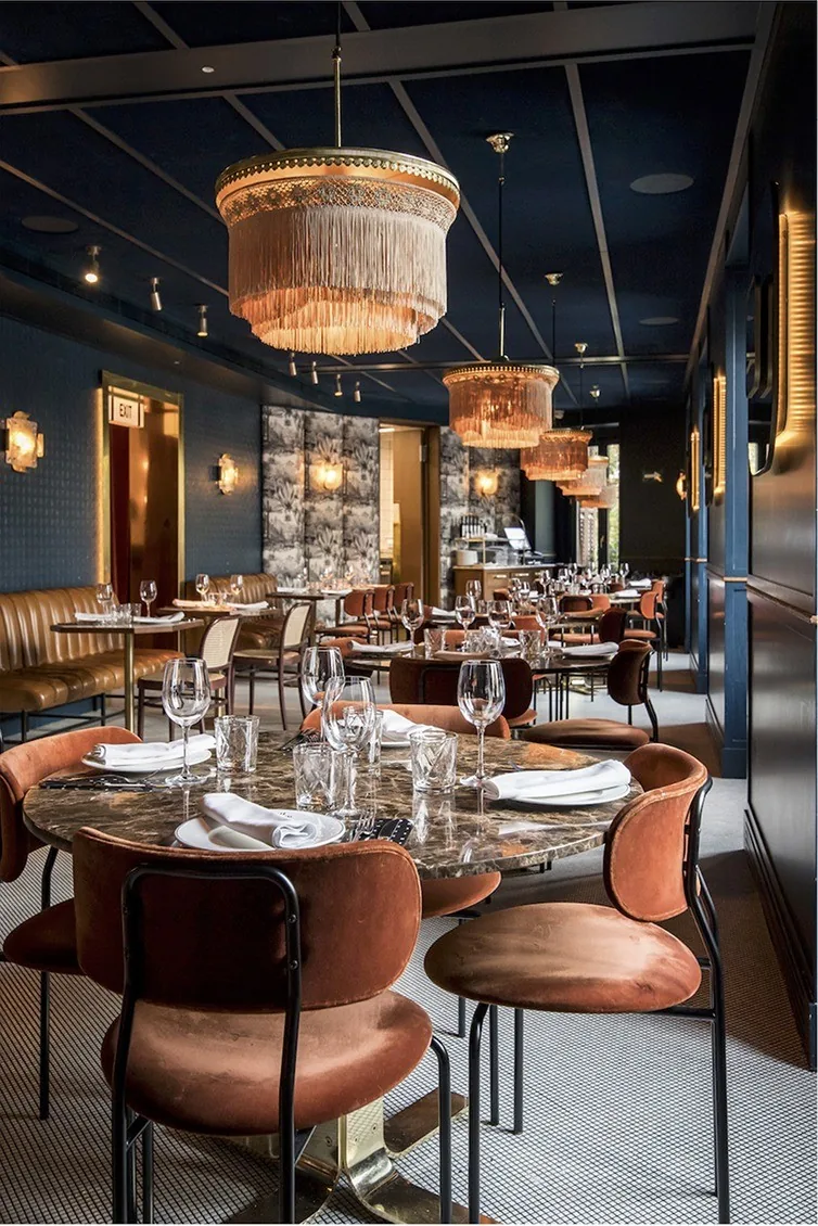 A cafe interior with blue walls, round tables, orange chairs and pendant lamps.