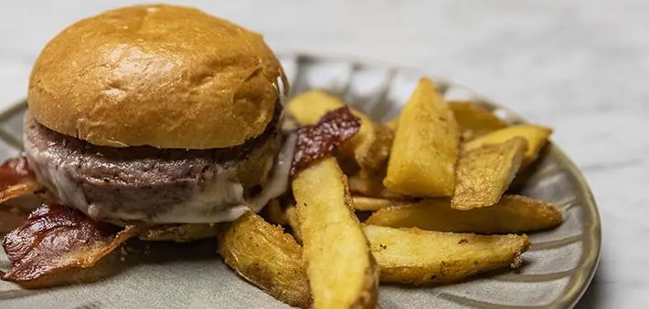 A cheeseburger with bacon and thick-cut chips on a ceramic plate