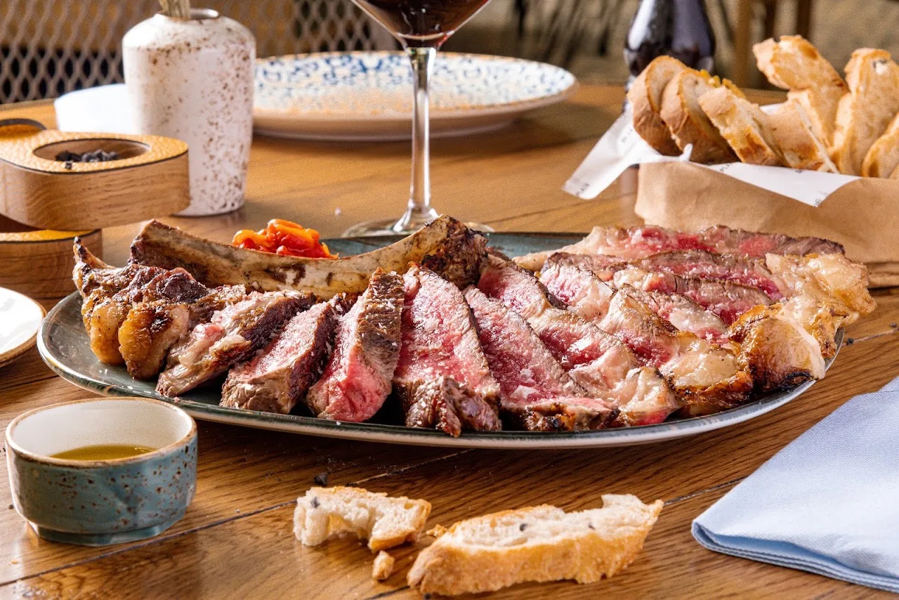 A platter of sliced steak with bread and dipping sauces