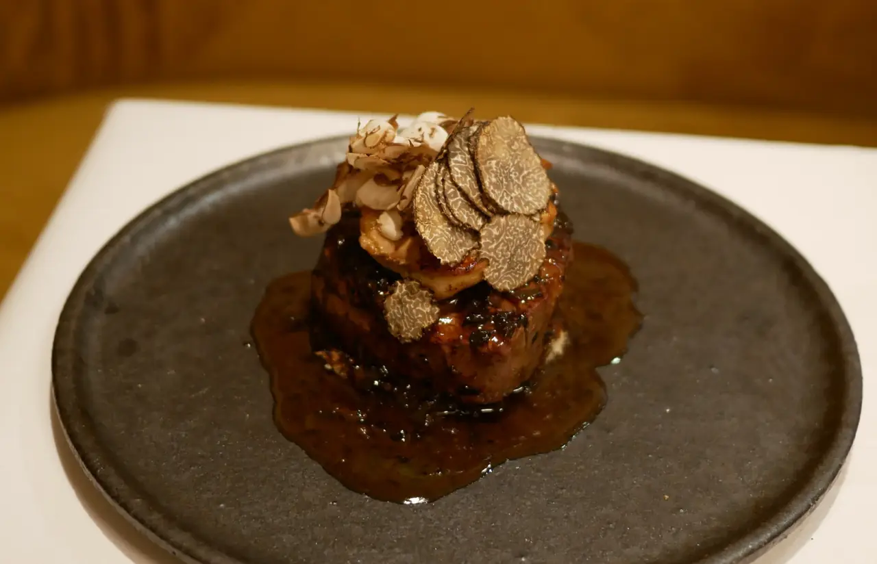 Seared meat topped with sliced black truffle and mushroom on a dark stoneware plate, finished with a rich pan sauce, at Cafe de Paris