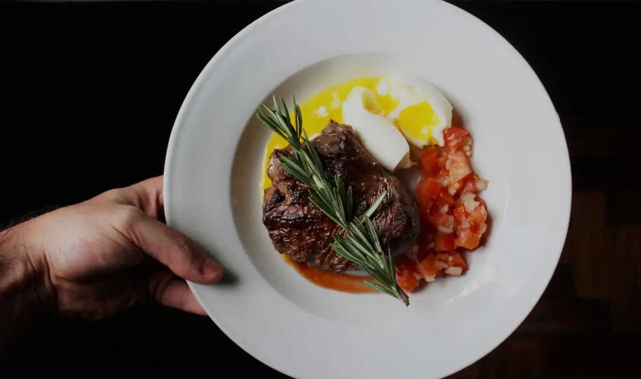 Grilled steak with a rosemary sprig, a poached egg in butter sauce, and diced tomato on a white plate, at Cafe de Paris