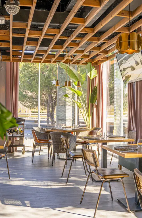 Dining room interior with woven rattan chairs, wooden slat ceiling, tropical plants and floor-to-ceiling windows