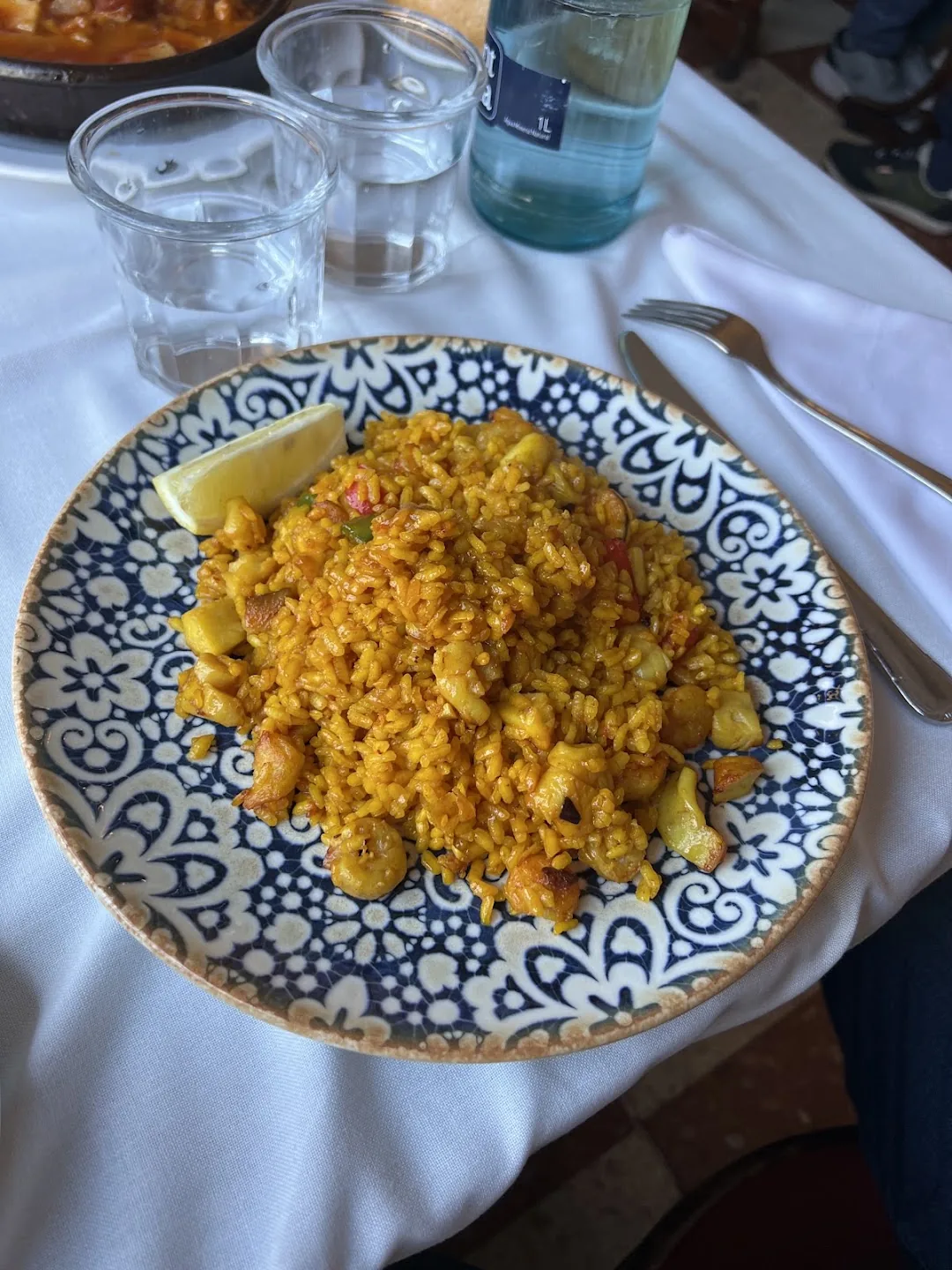 A saffron-yellow rice dish studded with shrimp and diced ingredients, served with a lemon wedge on a blue-and-white patterned plate