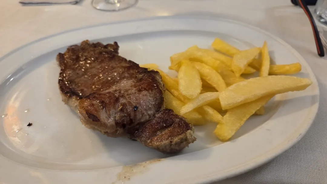 A grilled steak served with a portion of golden french fries on a white oval plate