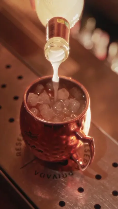 A drink being poured into a copper mug over ice