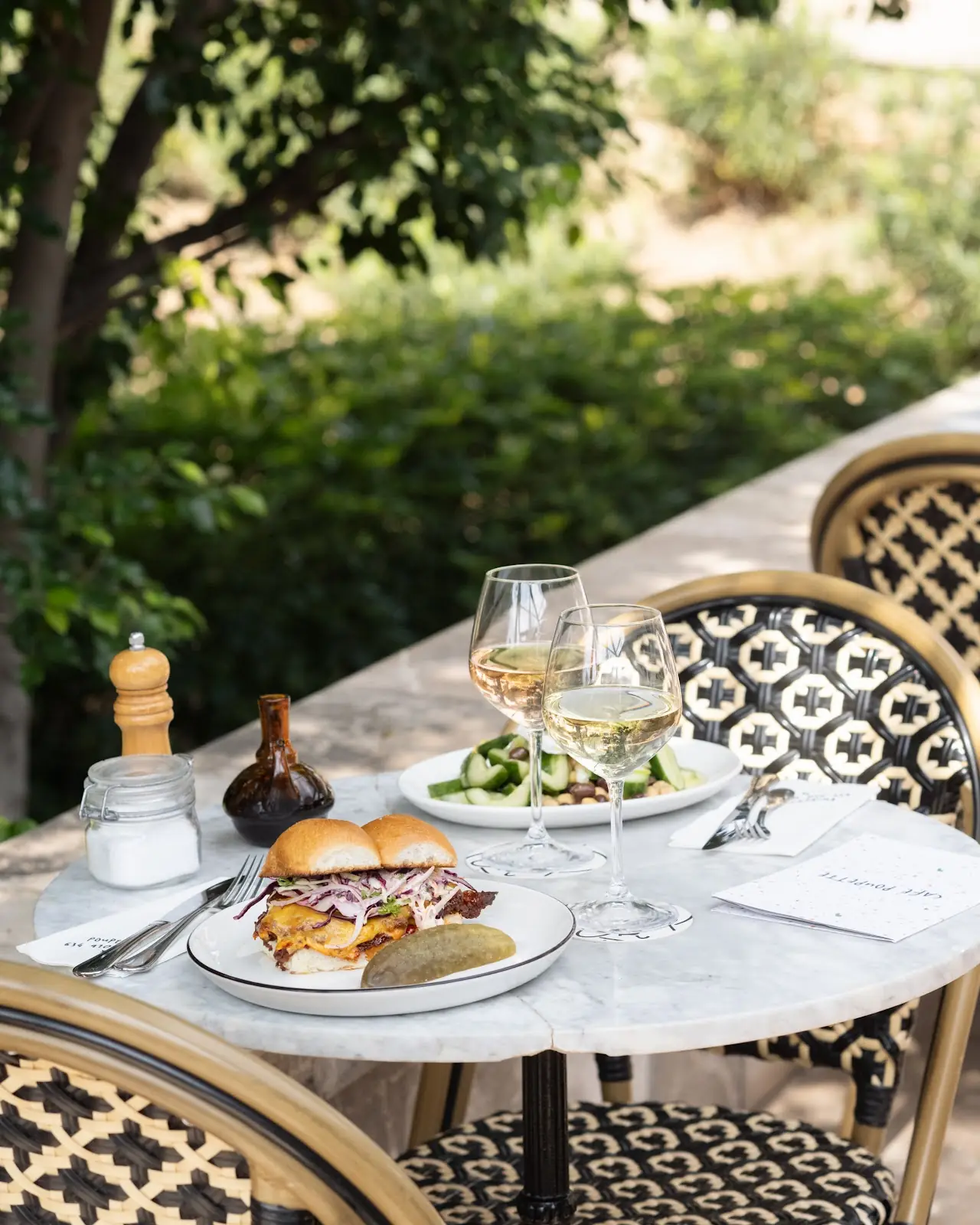 A burger and a glass of white wine on a marble terrace table by the park