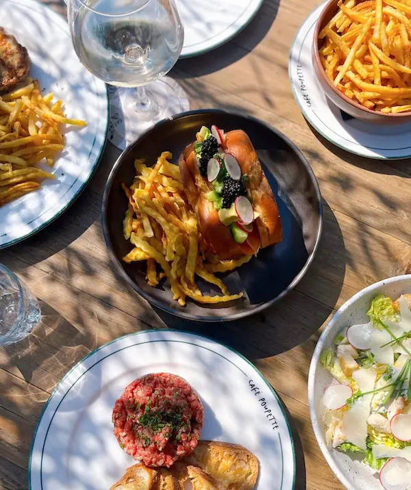 A sando with fries, a steak tartare and a side salad on a terrace table