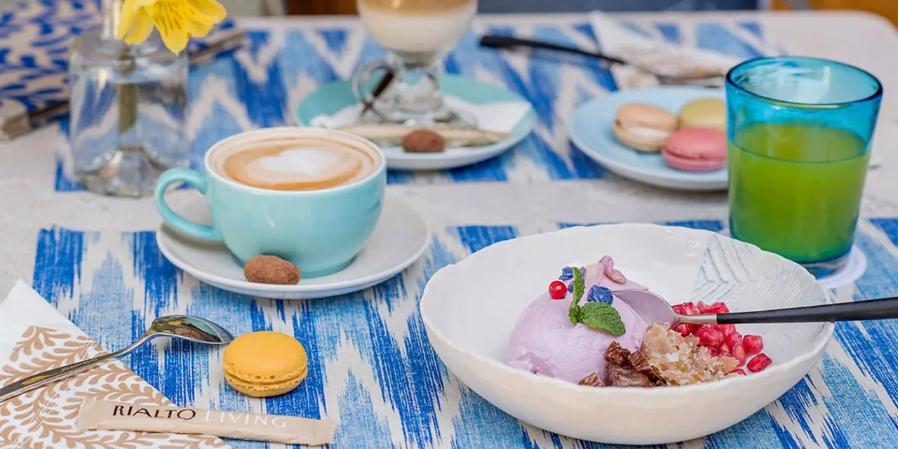 A cappuccino, a granola bowl and macarons on a blue-patterned table at Café Rialto