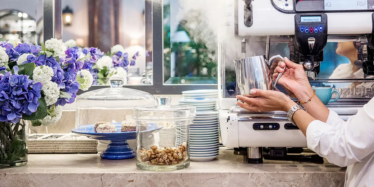 The café counter with cake domes, flowers and a barista at the espresso machine