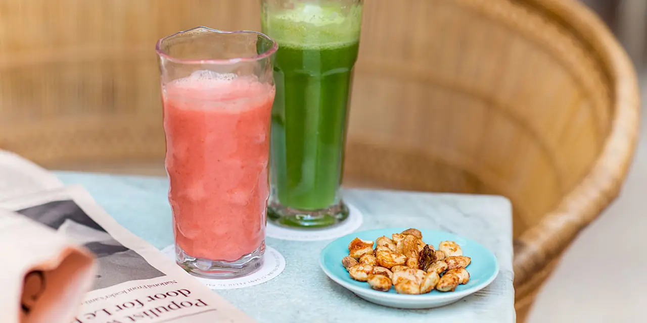 A pink juice and a green juice beside a small plate of snacks