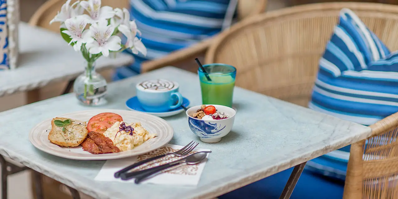A café table set with pastries, coffee cups and a small vase of flowers