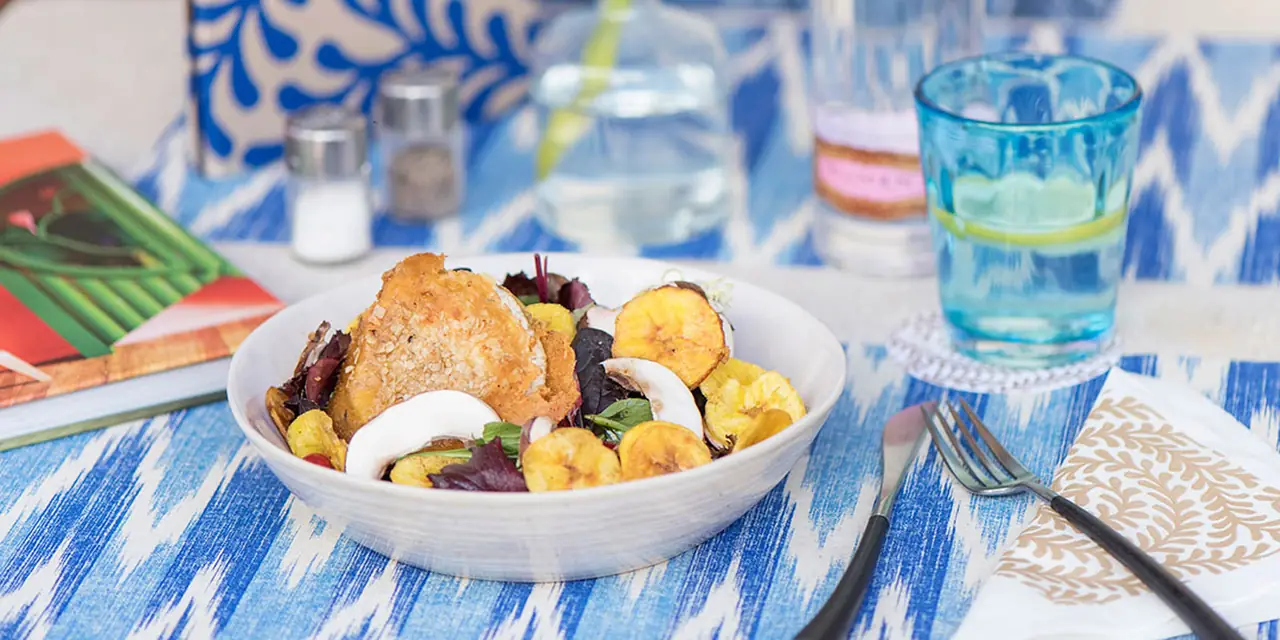 A lunch bowl with baked potatoes and greens on a blue-patterned table