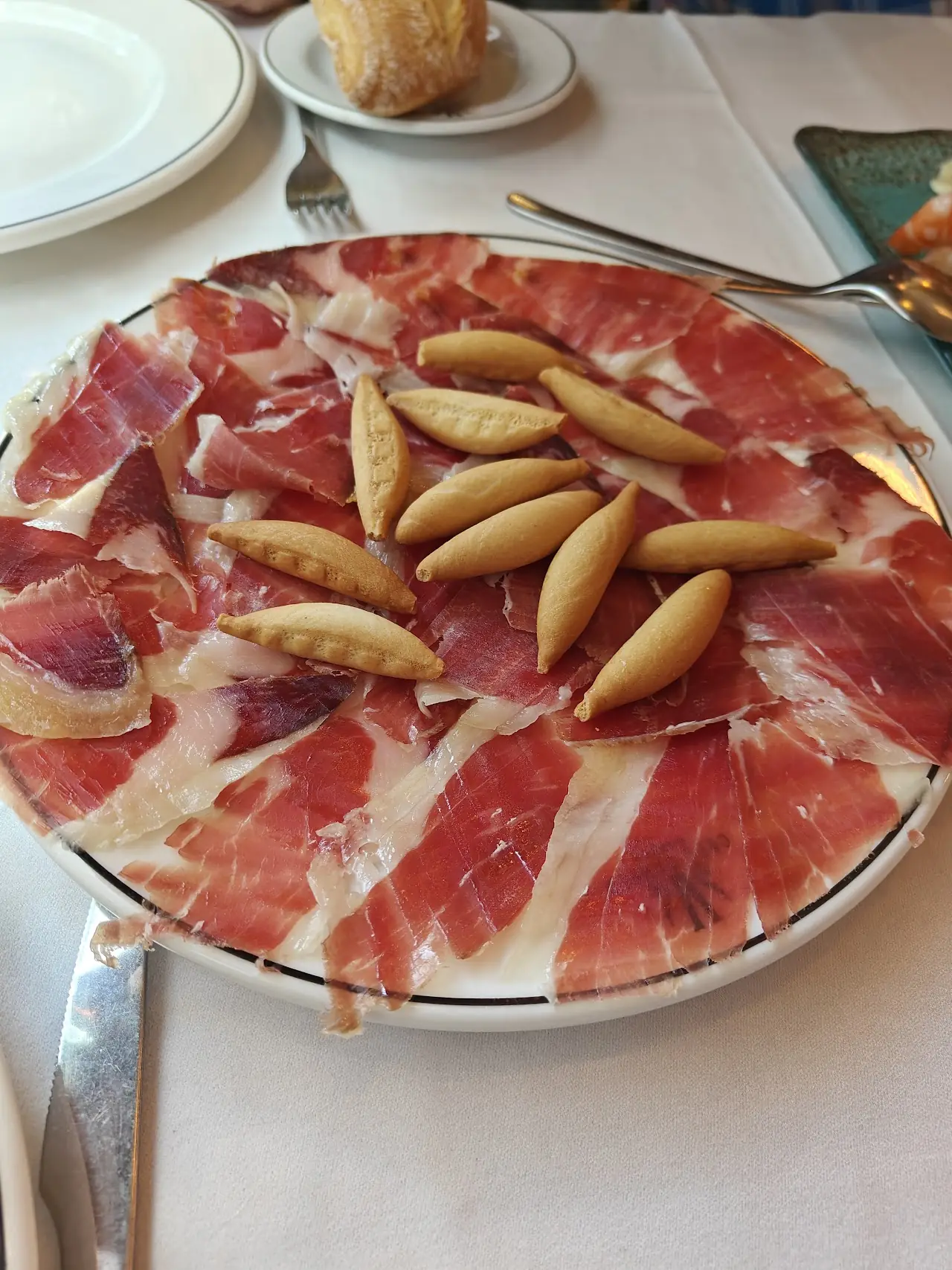 Sliced cured ham served with breadsticks.