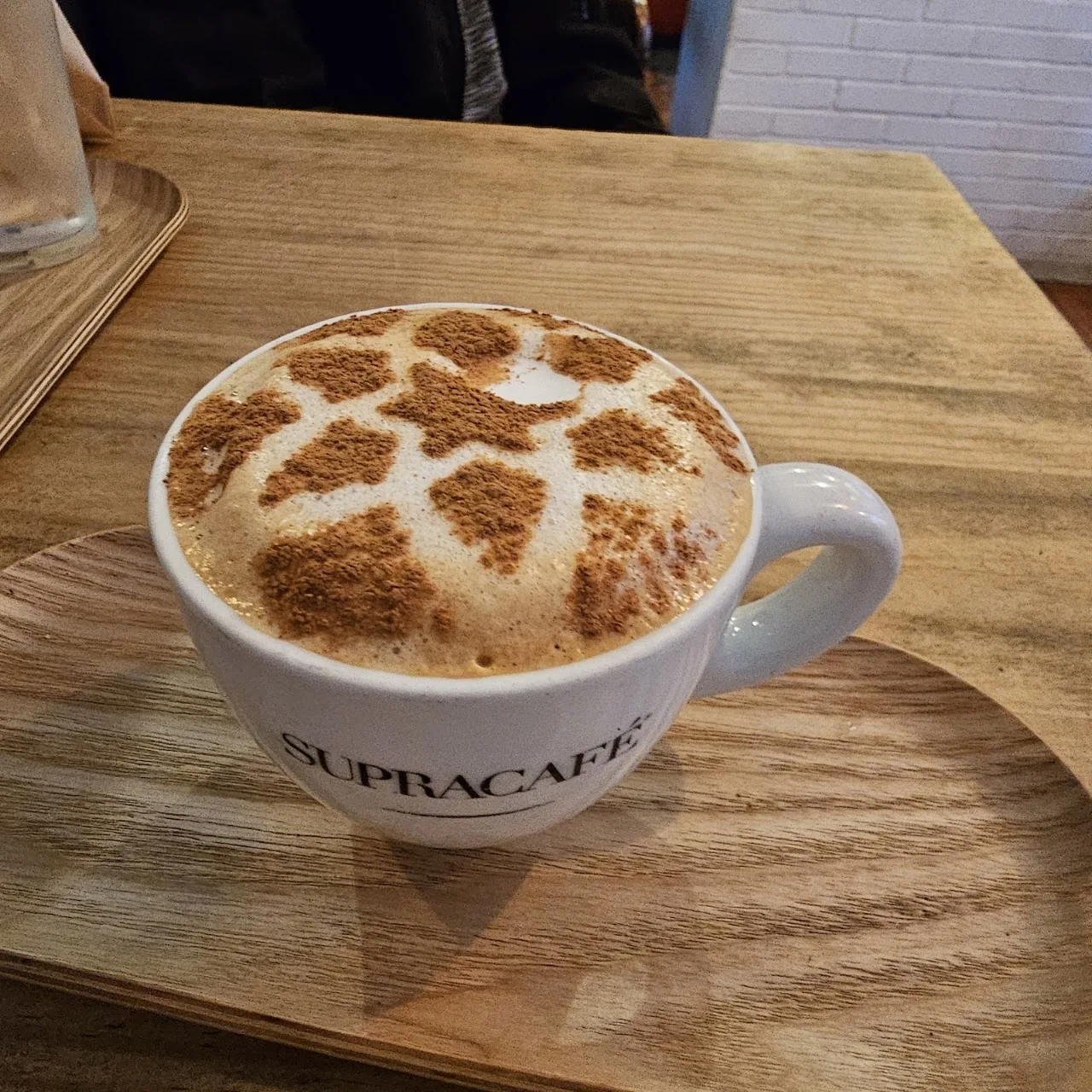 A cappuccino with leaf-patterned latte art in a cup labeled Supracafe