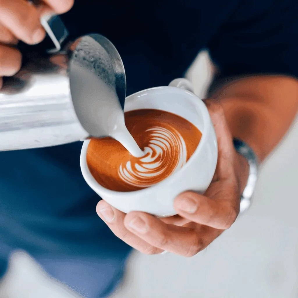 A hand holding a cup while milk is poured to make latte art