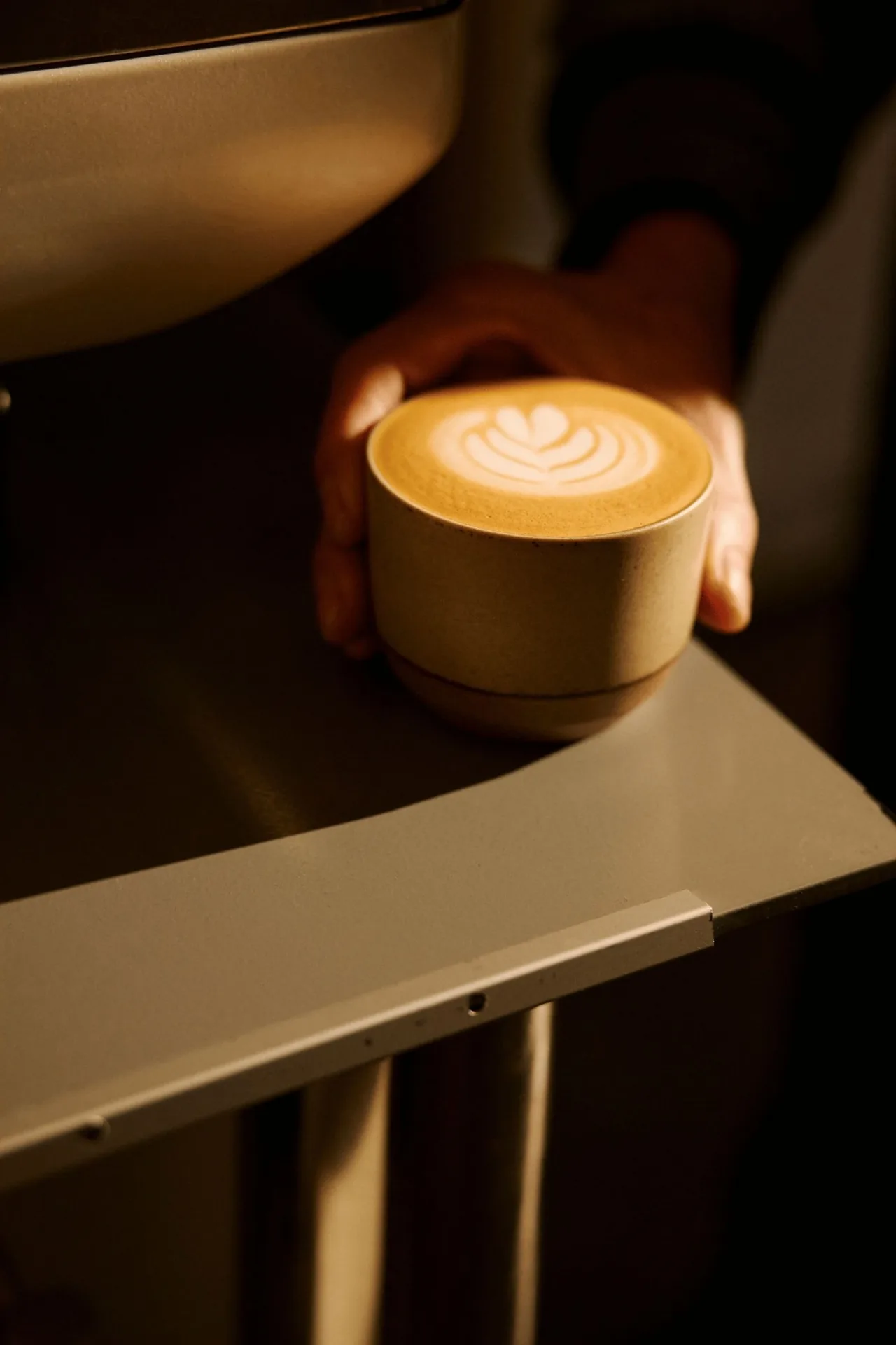 A hand holding a small cup of latte with art on a dark counter