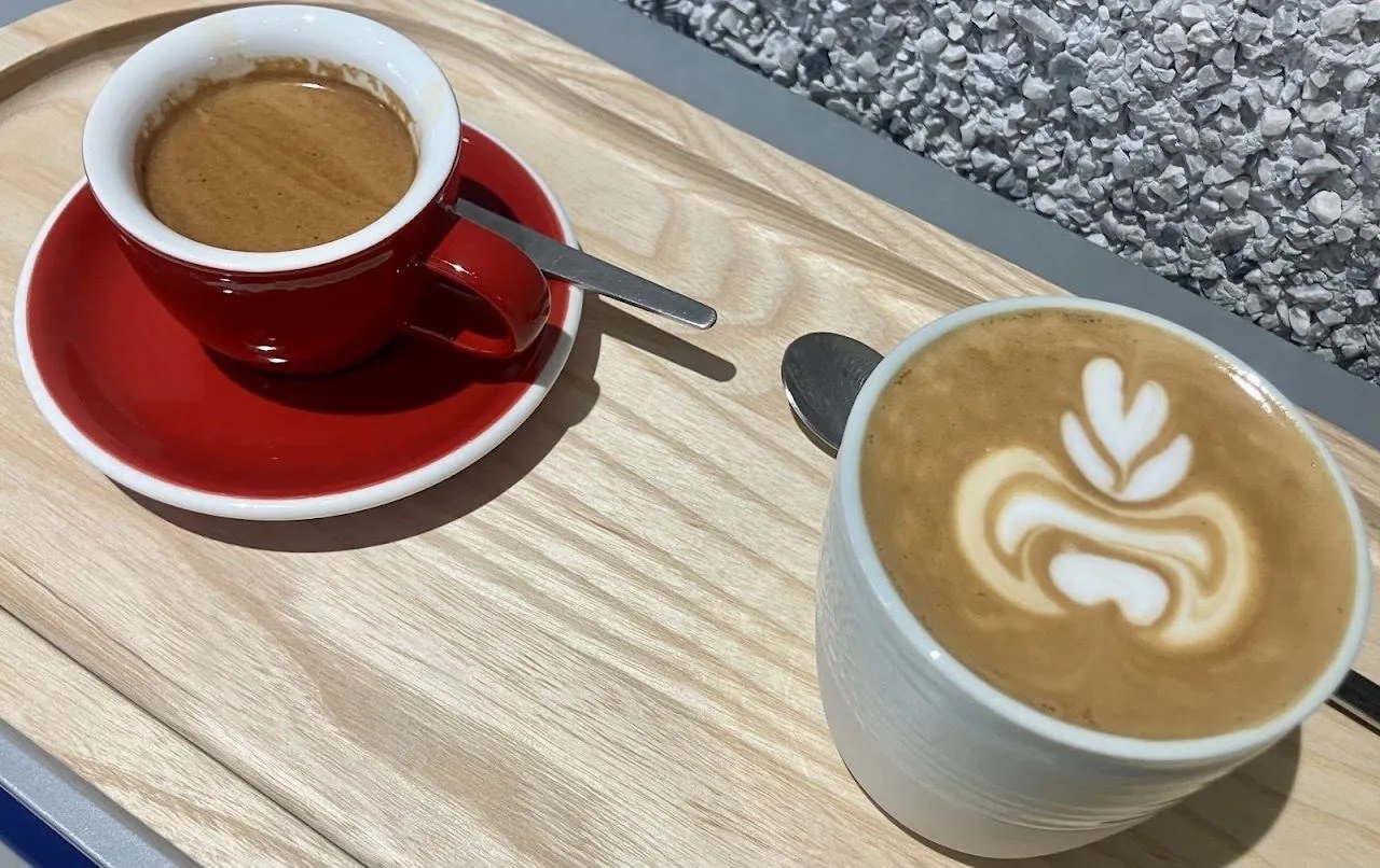 A latte and a small coffee in red and white cups on a wooden tray