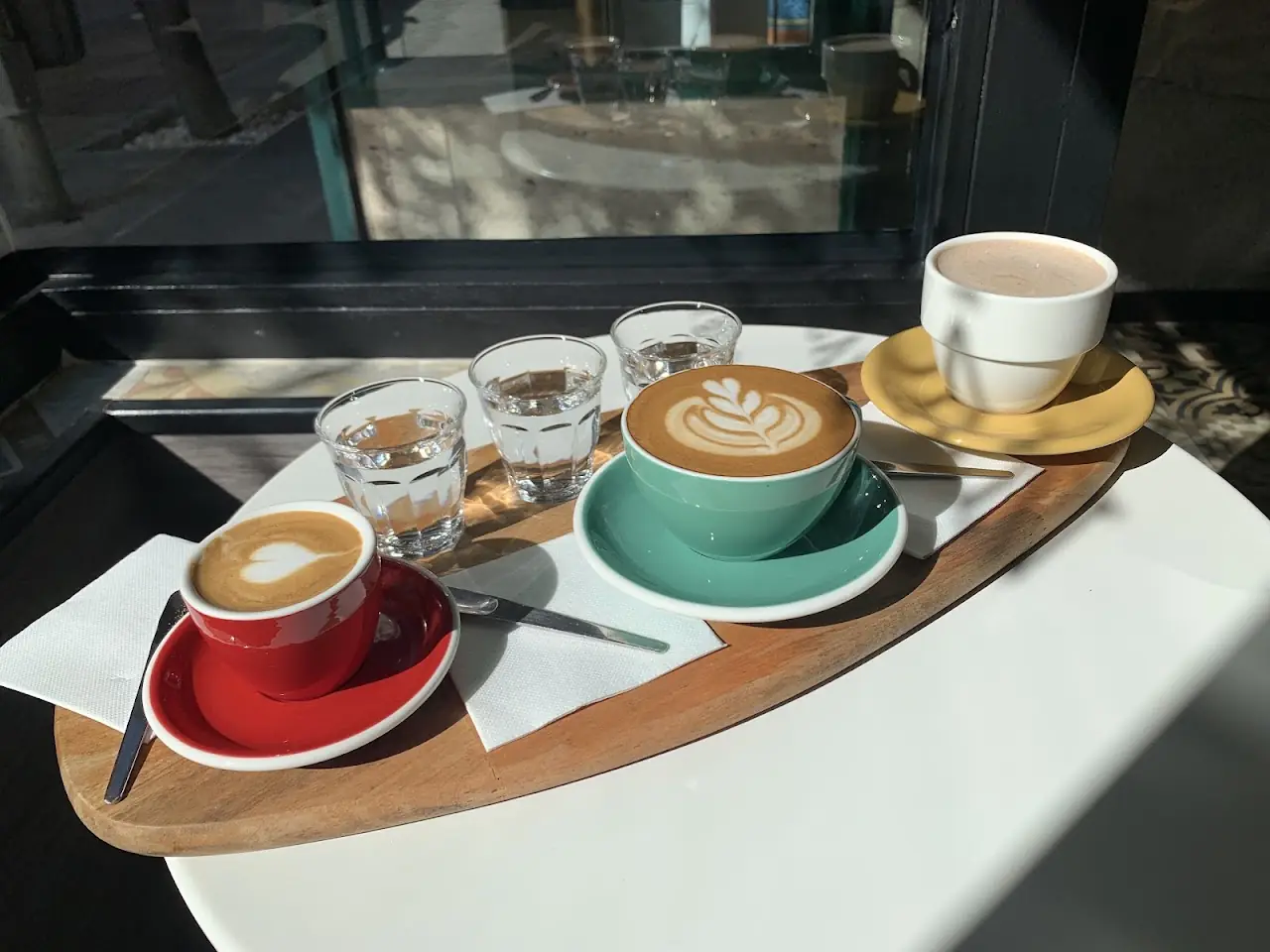 A tasting flight of coffee drinks including latte art and espresso, on a wooden board.