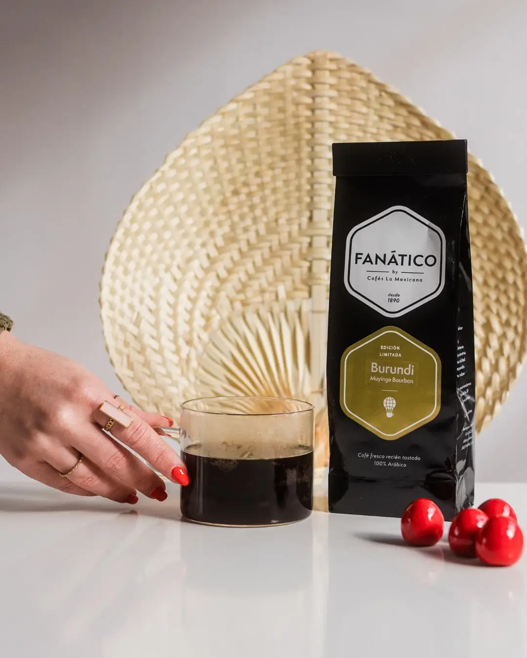 Hand reaching for a small cup of black coffee next to a bag of Fanatico Burundi coffee and cherries