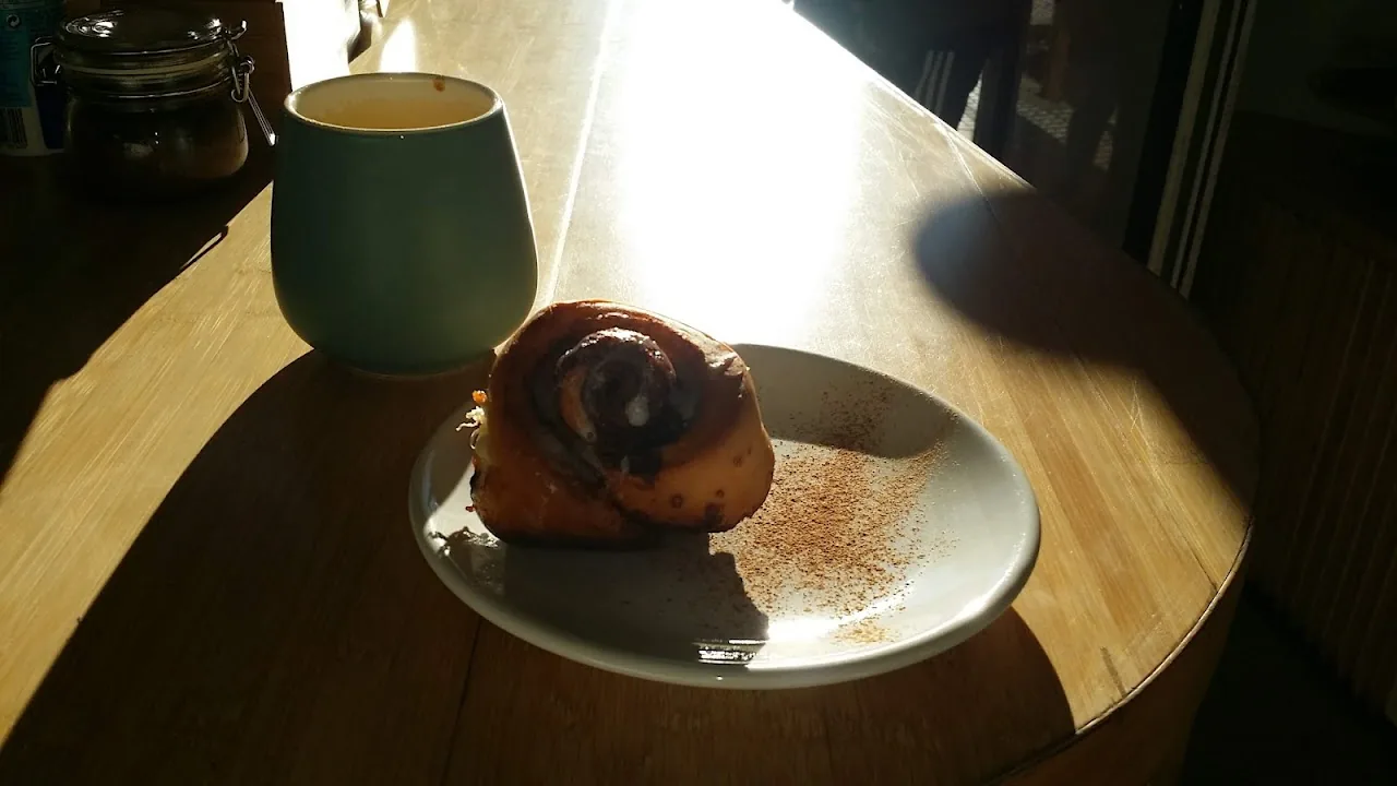 A round pastry with a swirl top on a plate beside a coffee mug