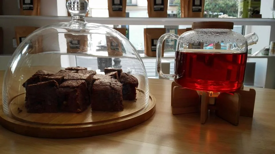 Brownie squares under a glass dome beside a glass of iced tea