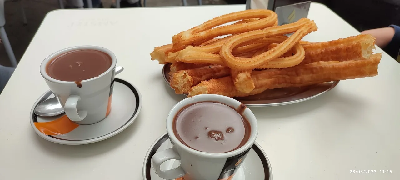 A plate of churros beside two cups of hot chocolate on a white table