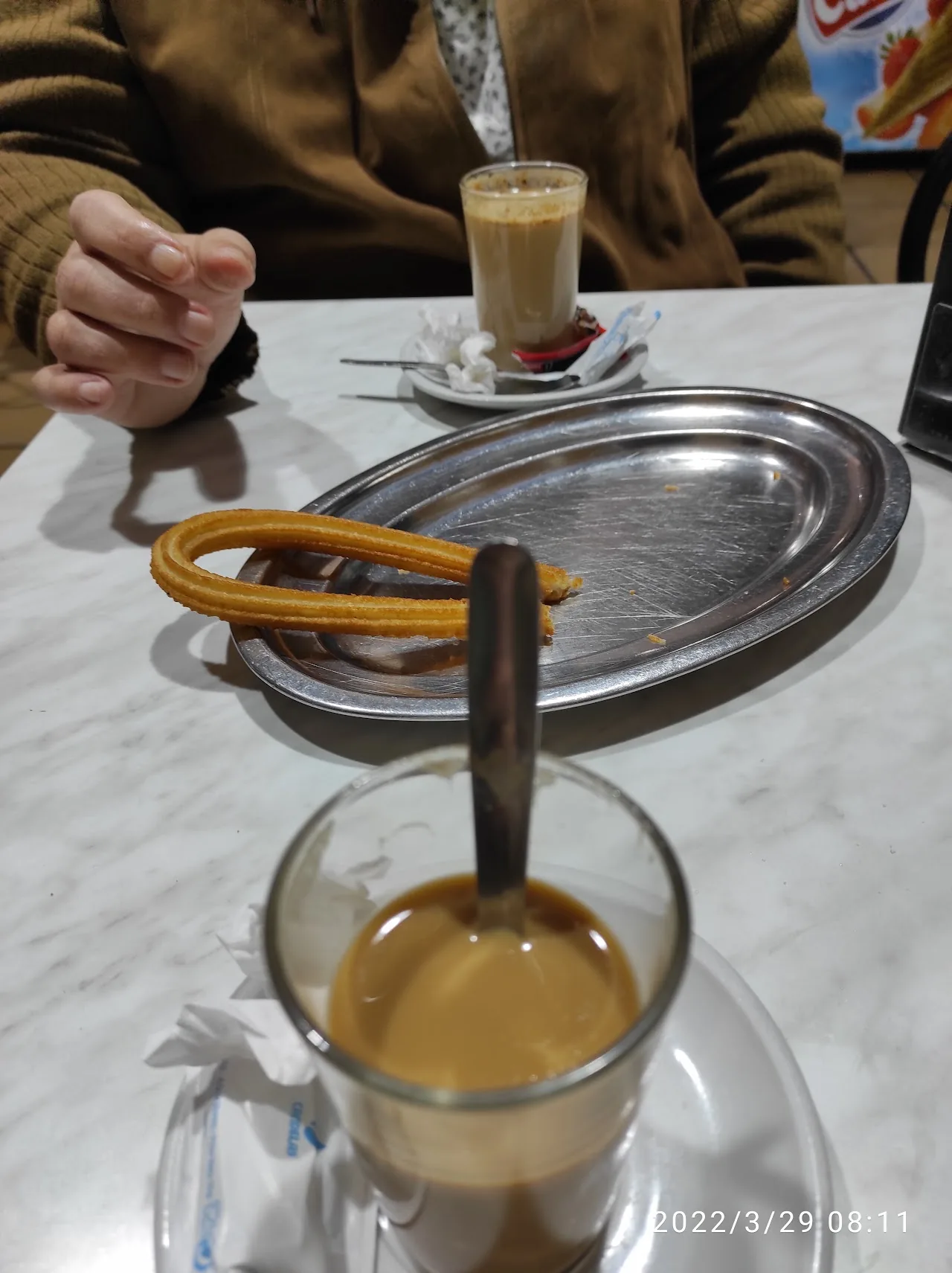 A churro dipped into a cup of coffee on a metal tray
