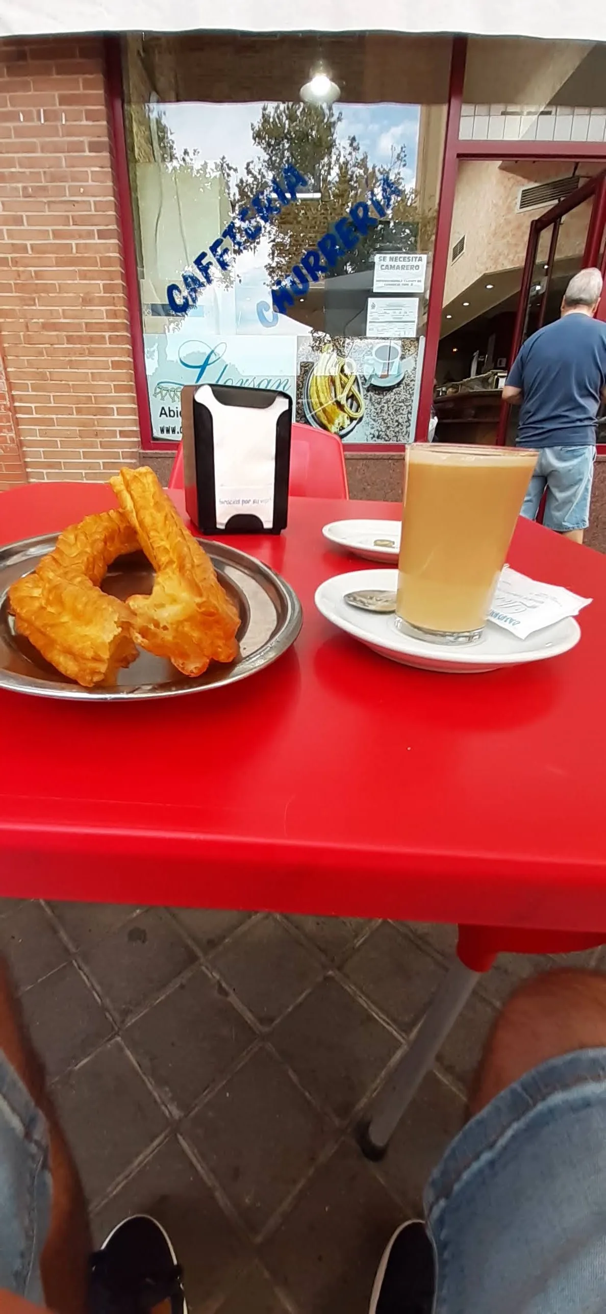 A plate of churros beside a coffee cup on a red table