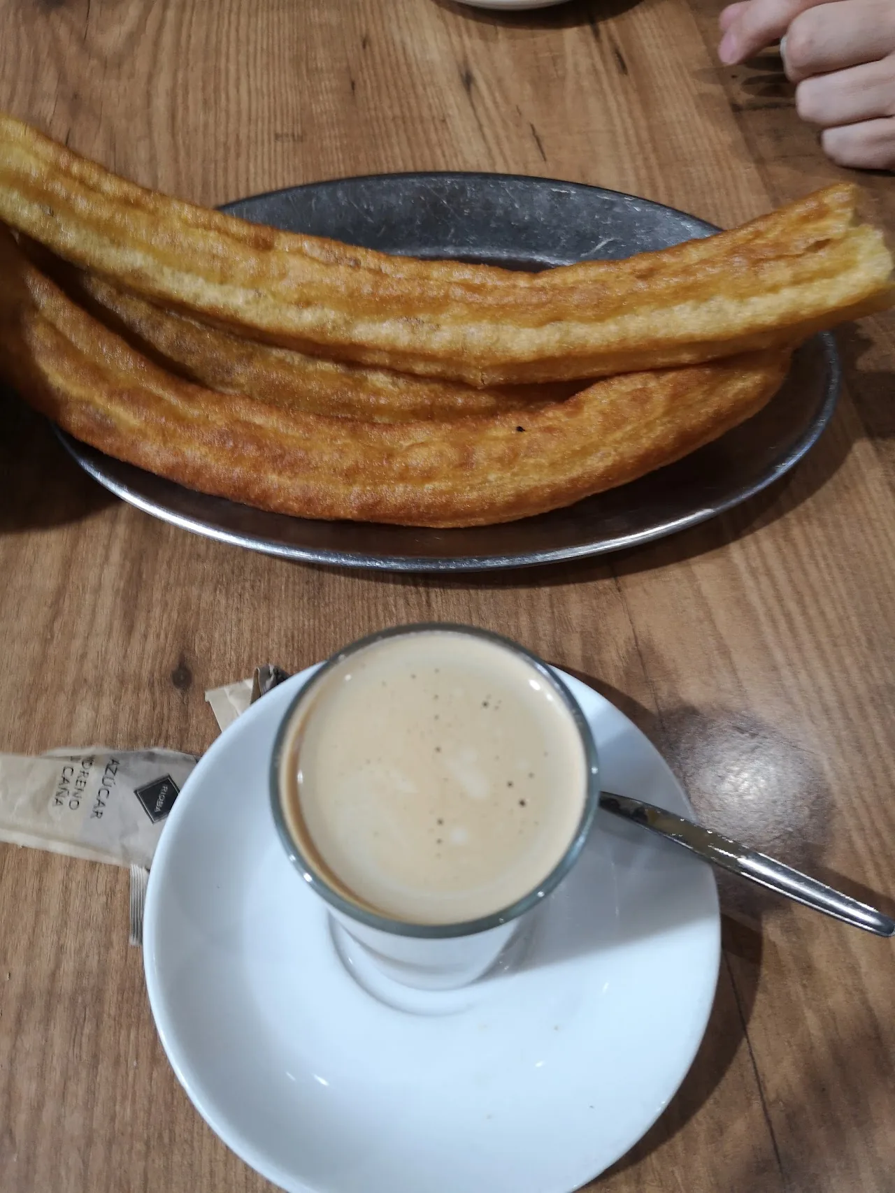 Churros on a metal tray next to a small coffee cup