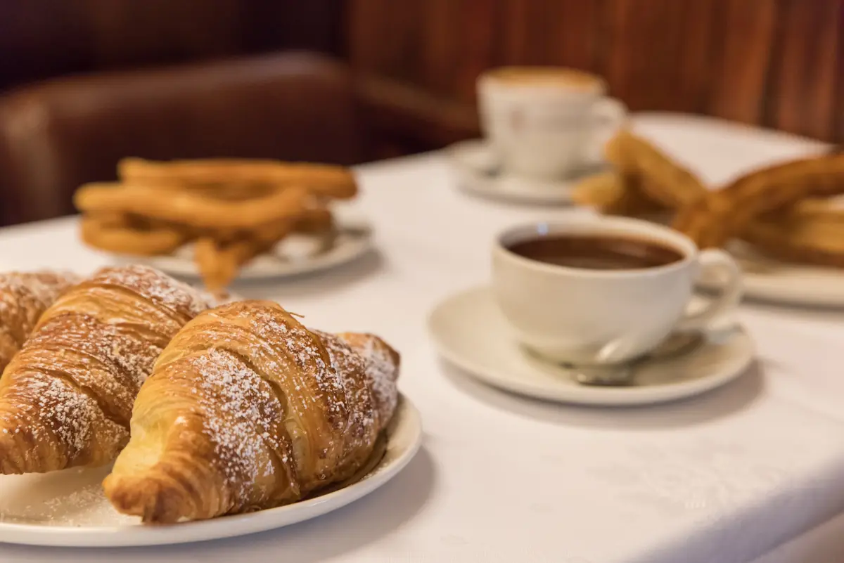 Powdered-sugar croissants, churros and cups of hot chocolate and coffee on a table