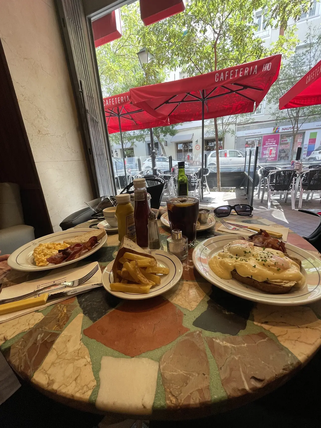 Table spread with scrambled eggs and bacon, fries, eggs Benedict-style toast and iced coffee