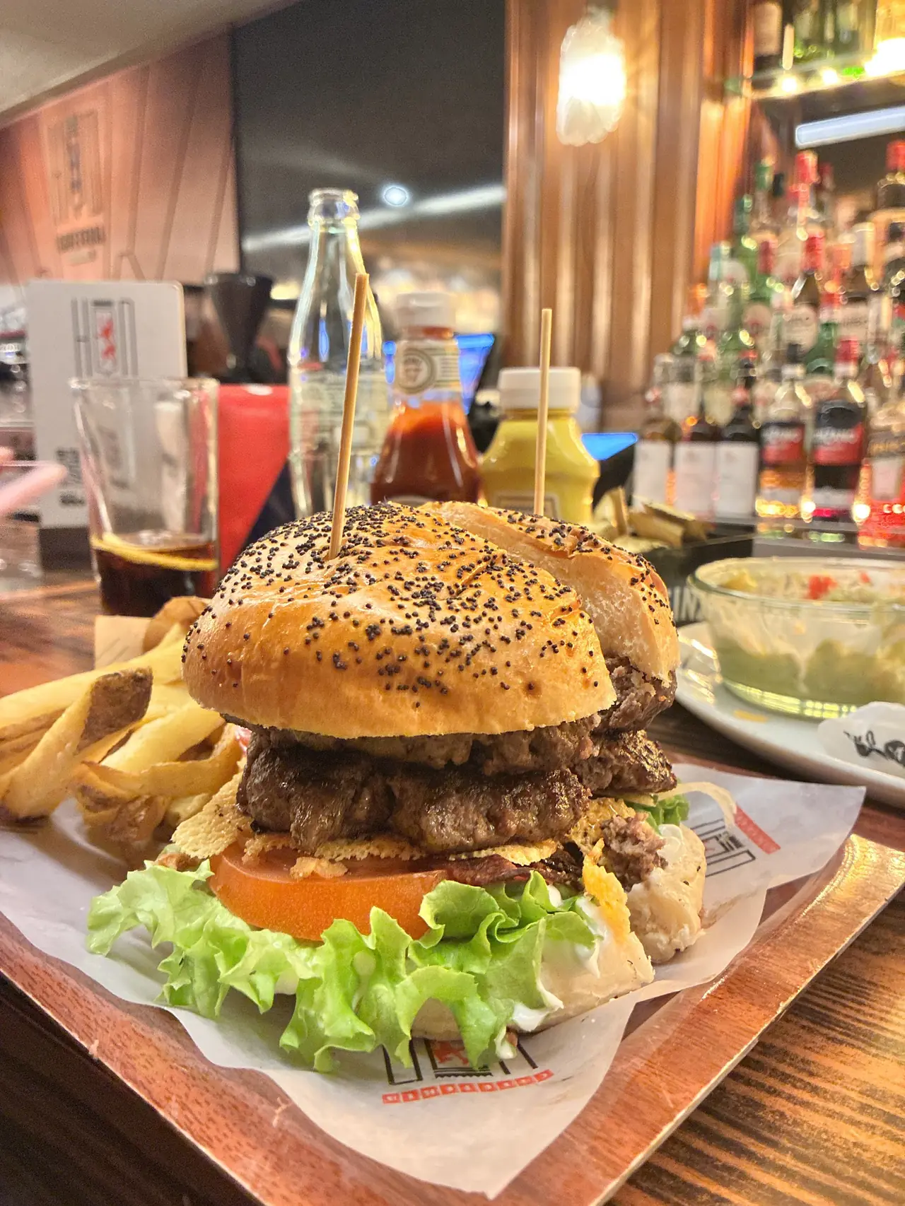 Double stacked poppy-seed bun burger with lettuce and tomato, served with fries at the bar