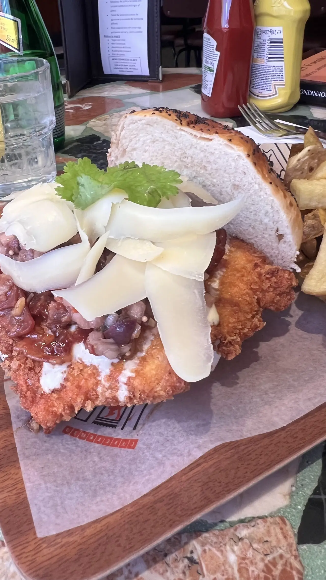 Fried chicken sandwich topped with shaved cheese and cilantro, served with fries