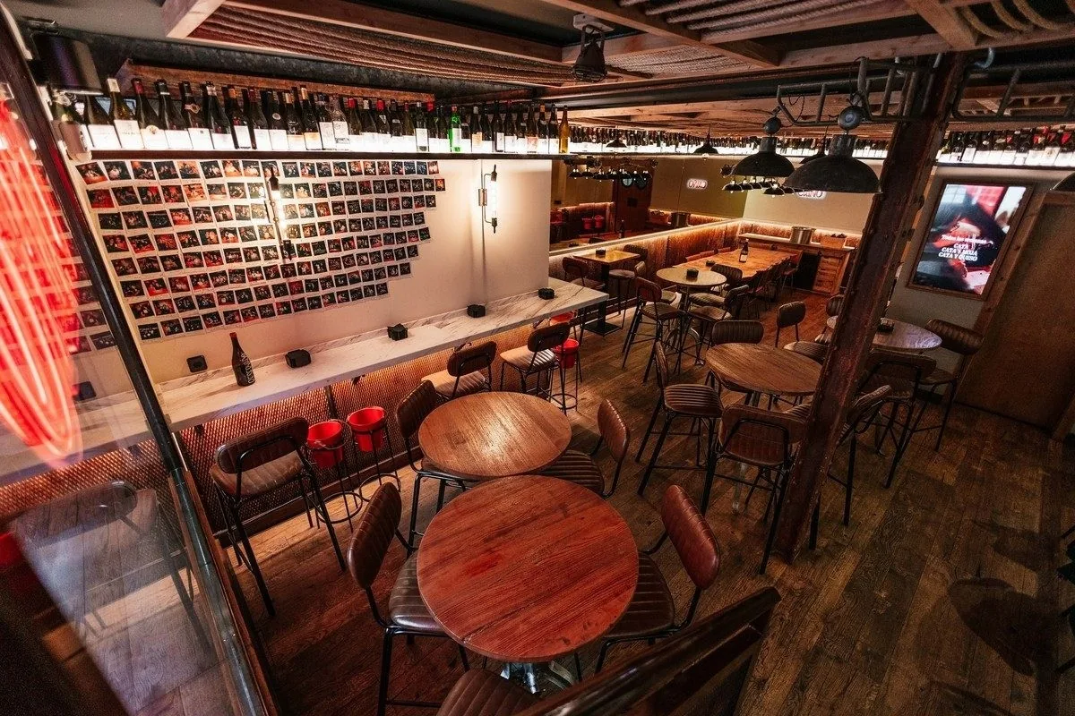 A wine bar dining room with red tables, wooden floor and shelves of bottles