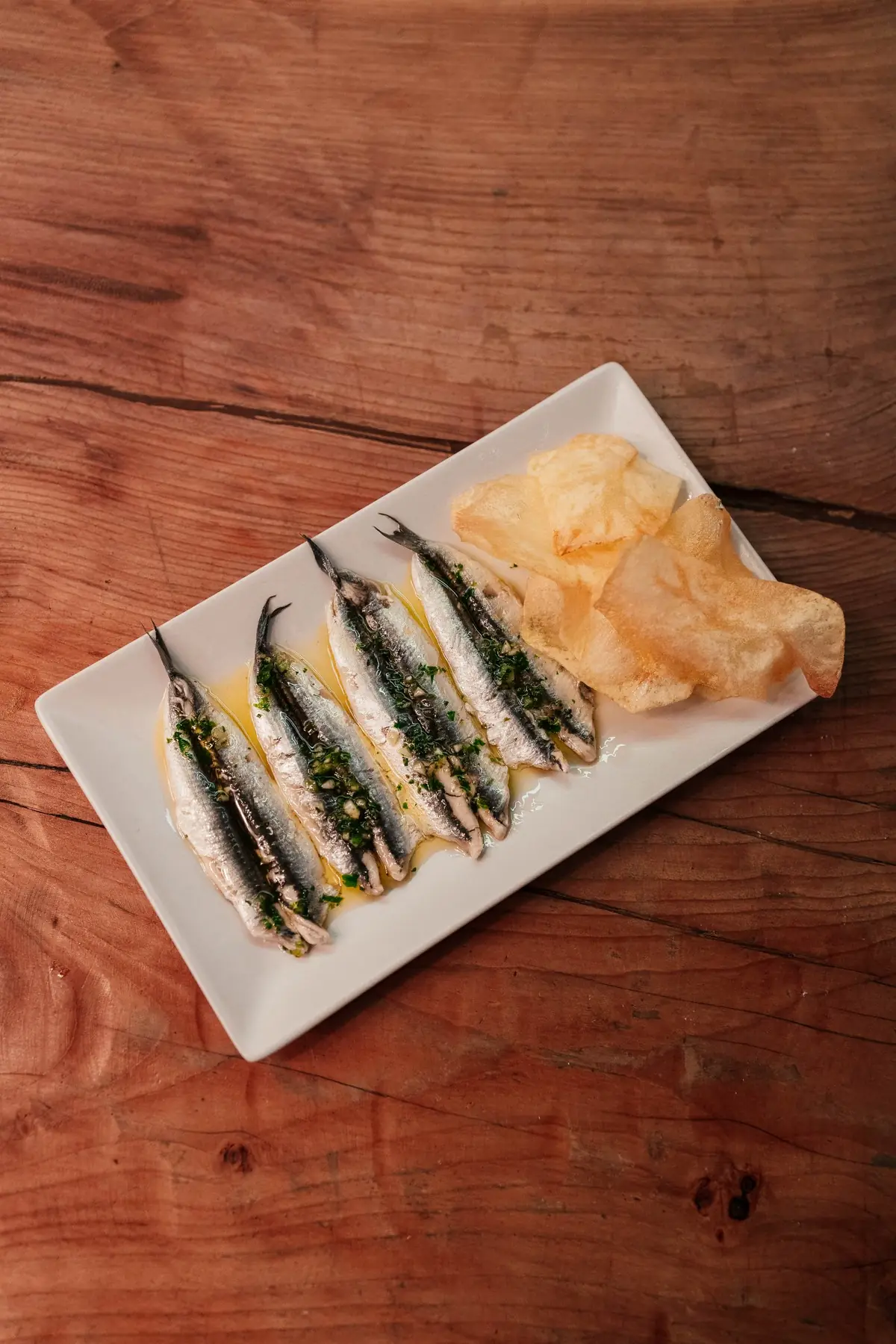 Marinated anchovy fillets on a plate with a crisp.