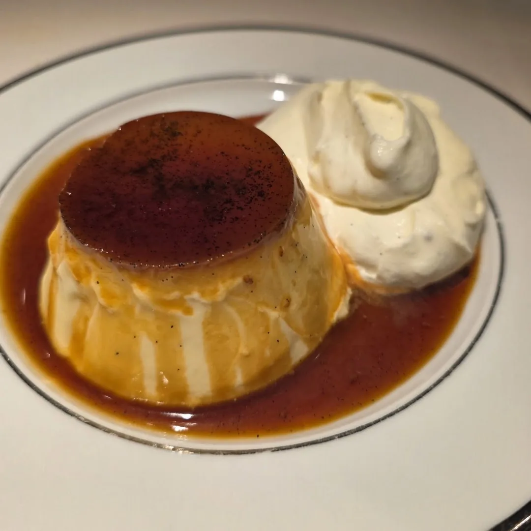A caramel flan with a scoop of whipped cream on a plate pooled with caramel sauce