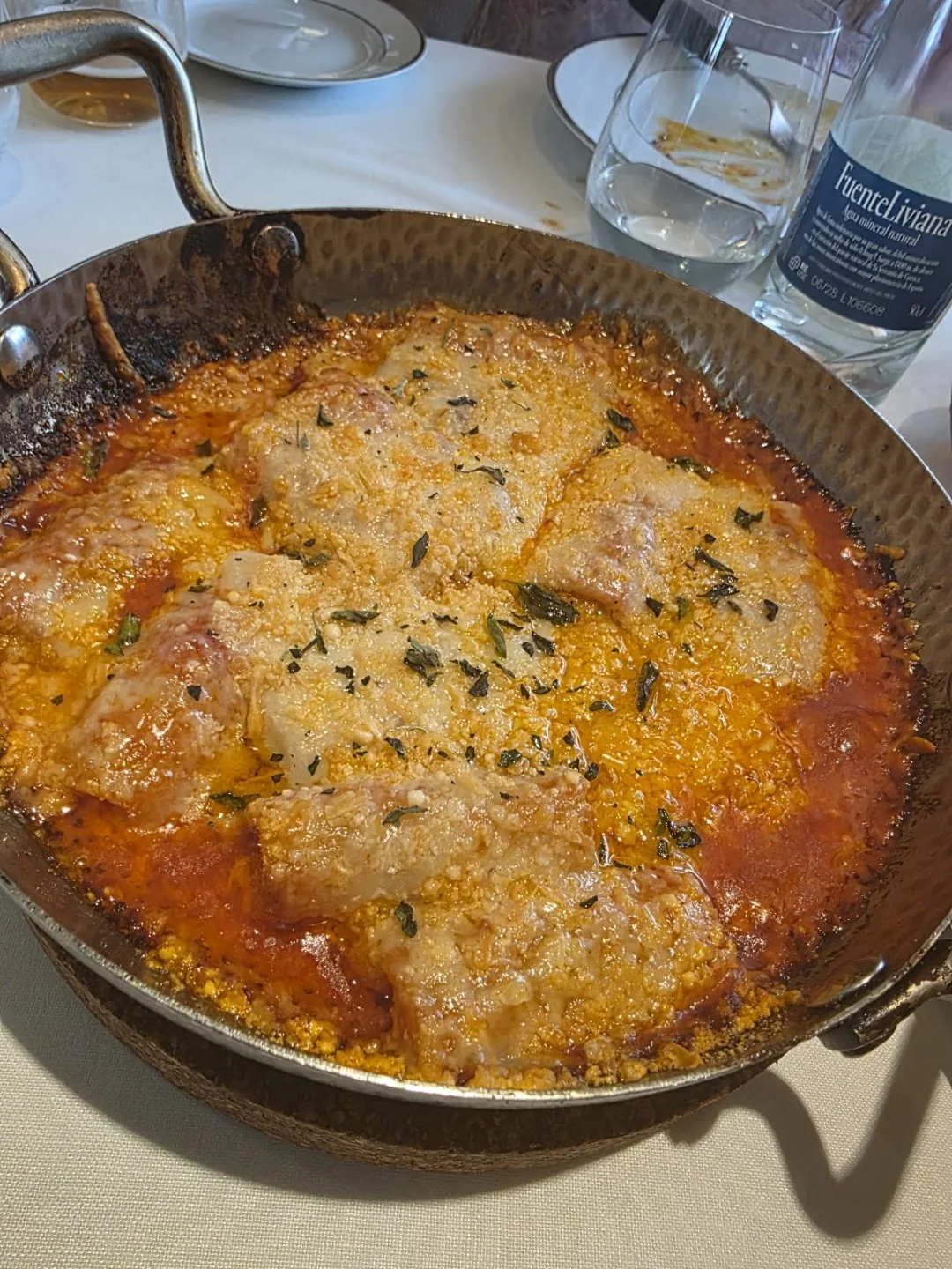 A pan of breaded fish fillets baked with tomato sauce, melted cheese and herbs
