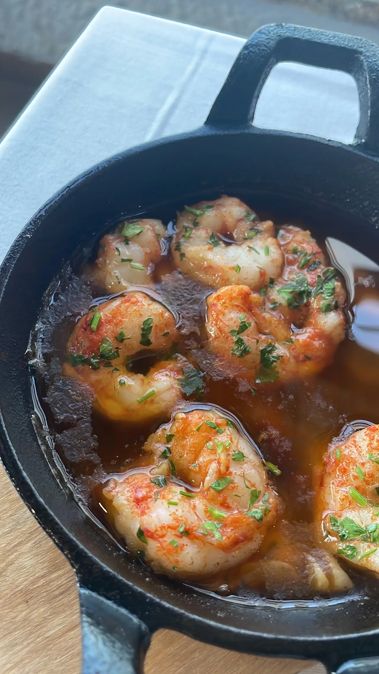 Garlic shrimp sizzling in oil in a small black pan.