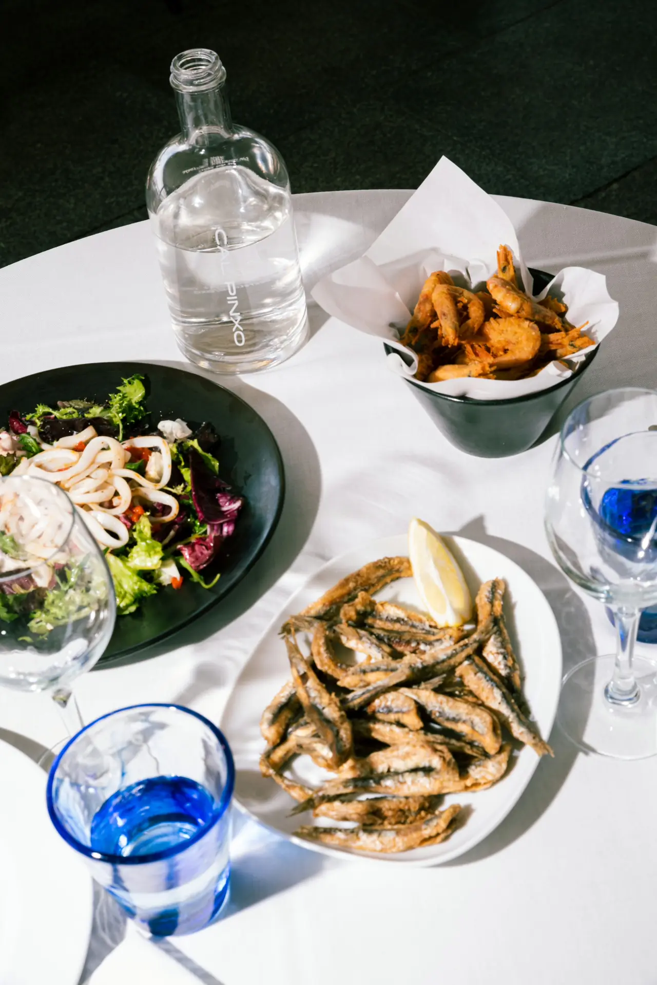 Fried anchovies with a lemon wedge, an octopus and squid salad, and crispy fried shrimp on a white-clothed table at Cal Pinxo Palau de Mar