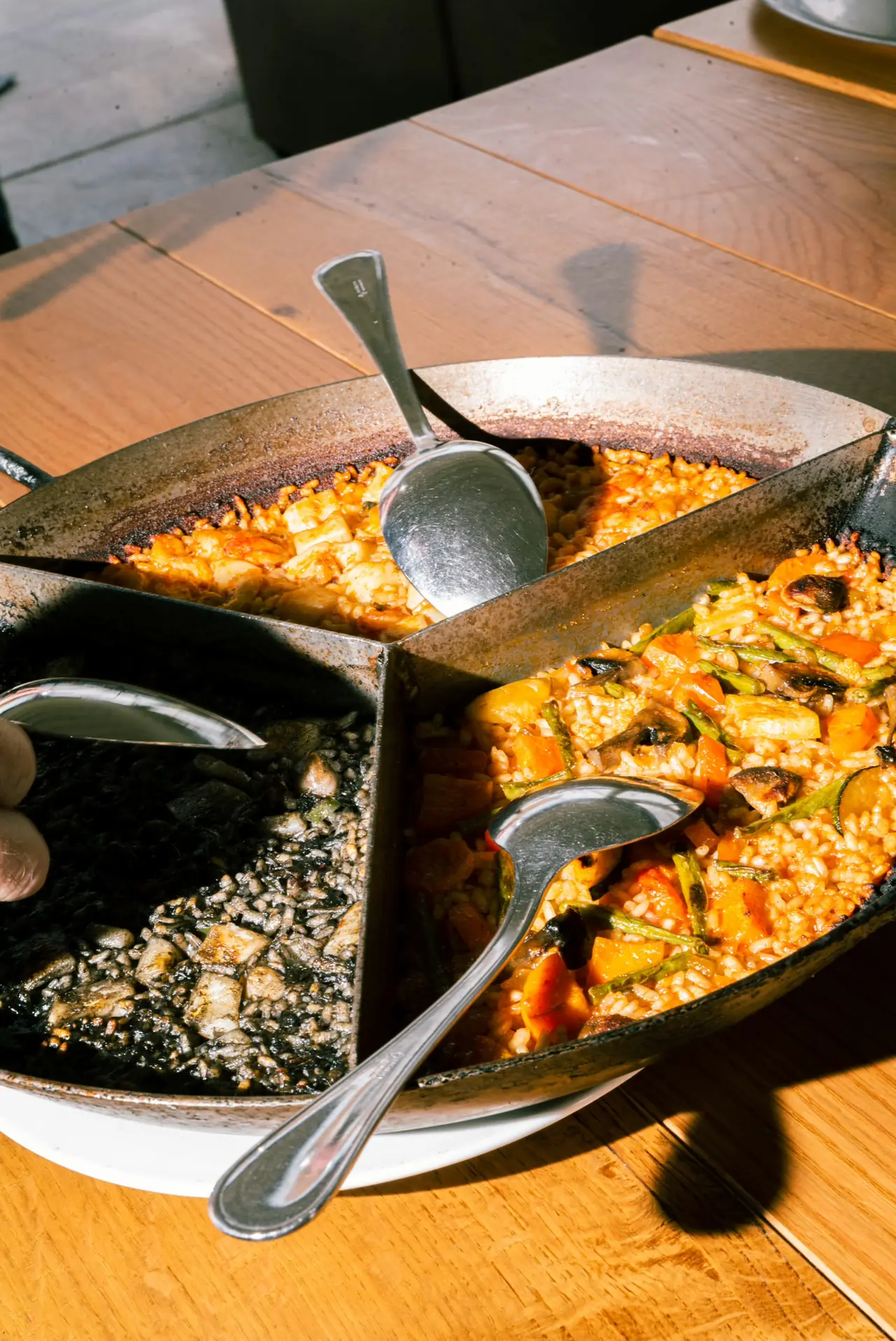 Two paella pans on a wooden table, one with black rice and one with mixed vegetable rice, at Cal Pinxo Palau de Mar