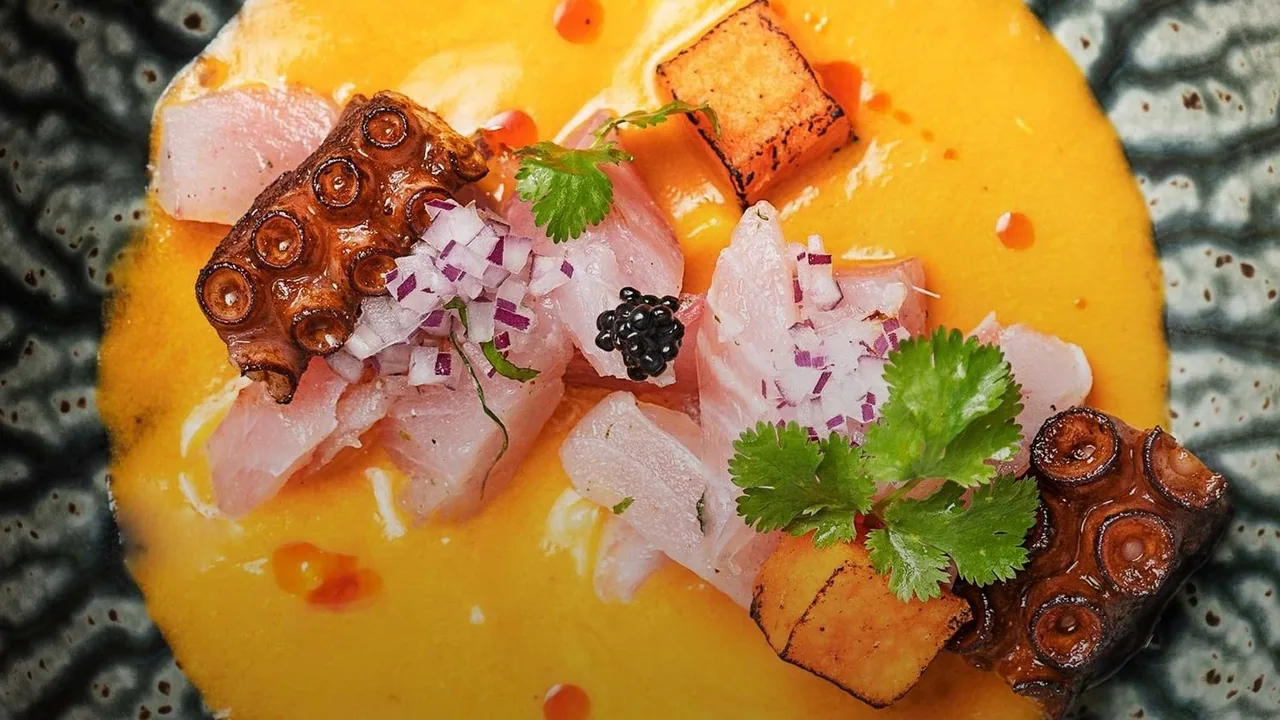 Slices of white fish and grilled octopus in a bright yellow sauce on a dark patterned plate