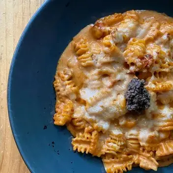 Ridged pasta in a creamy orange sauce topped with a dollop of black tapenade in a blue bowl