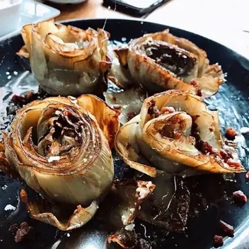 Roasted whole artichokes opened into flower shapes with crispy bits scattered on a dark plate